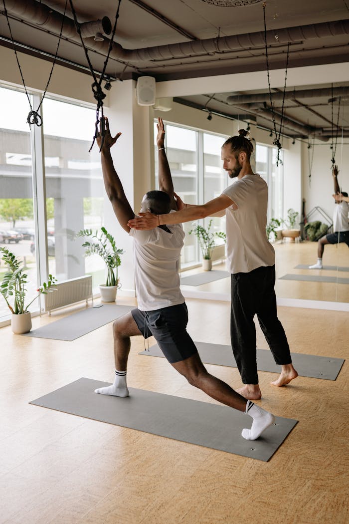 Instructor helps student with yoga pose in bright studio, promoting wellness and fitness.